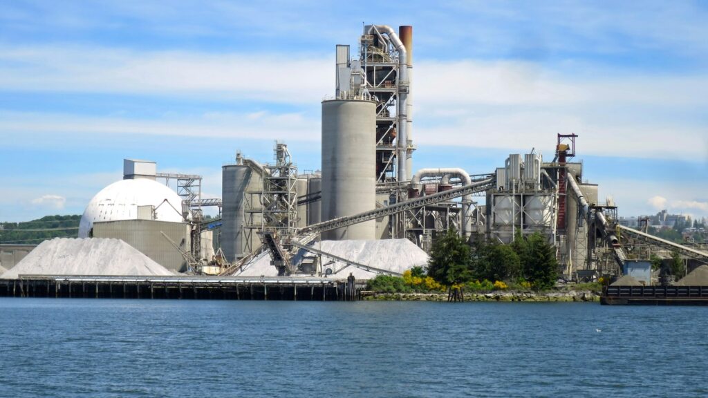 Cementfabrik med silor vid vattnet, illustrationsbild
