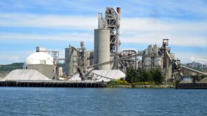 Cementfabrik med silor vid vattnet, illustrationsbild